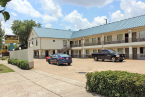 Two story building, exterior entrances to rooms with covered walkways and stairs, brand signage, parking spaces