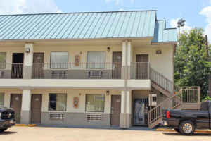 Two story building, exterior entrances to rooms with covered walkways and stairs, parking spaces