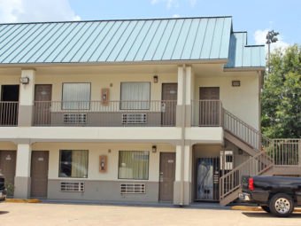 Two story building, exterior entrances to rooms with covered walkways and stairs, parking spaces