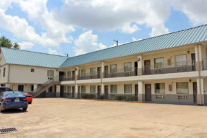 Two story building, exterior entrances to rooms with covered walkways and stairs, parking spaces