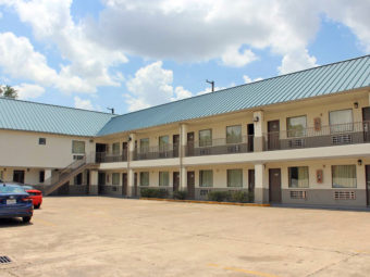 Two story building, exterior entrances to rooms with covered walkways and stairs, parking spaces