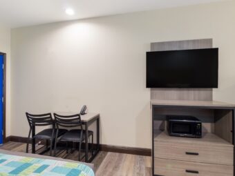 Small table with telephone and chairs, wooden drawer unit with microwave, wall mounted flatscreen TV, laminate flooring