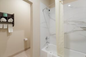 Wall shelf with towels, showertub with shower curtain and bath,at, tiled flooring