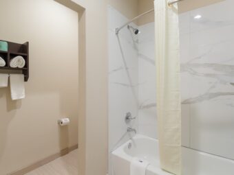 Wall shelf with towels, showertub with shower curtain and bath,at, tiled flooring