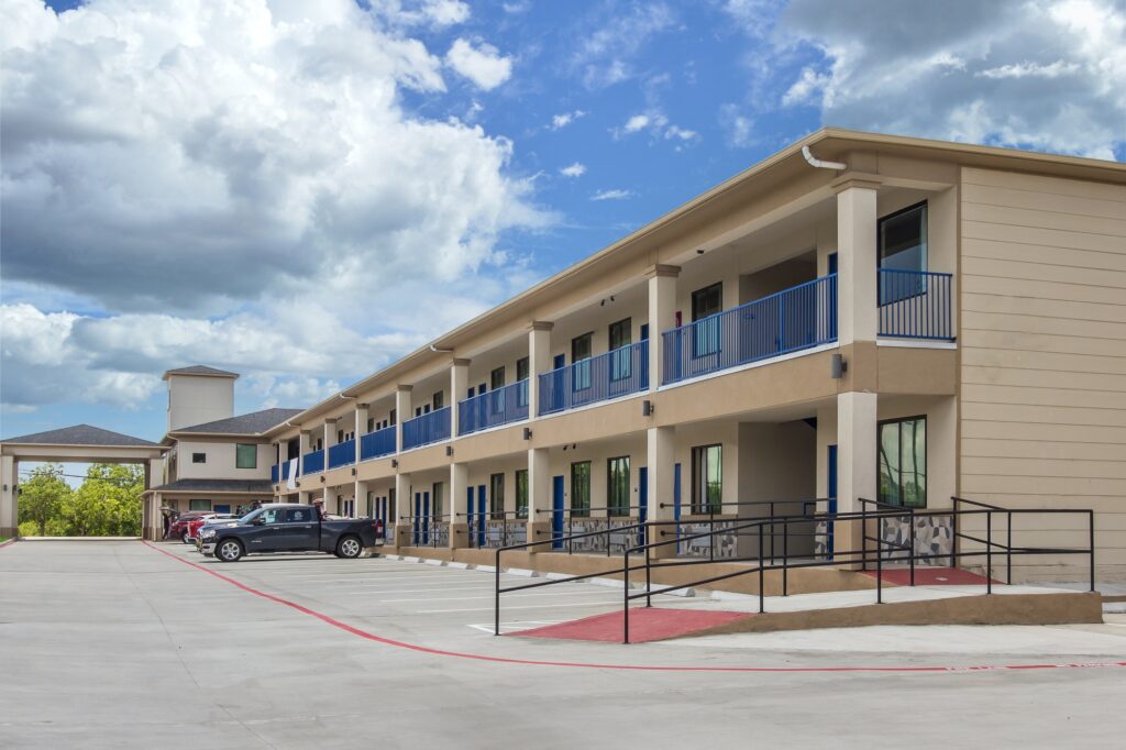 Two story building with external walkways and room entrances, wheelchair ramp with handrails, parking spaces