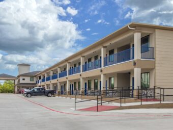 Two story building with external walkways and room entrances, wheelchair ramp with handrails, parking spaces