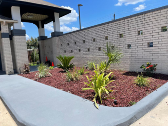 Landscaping with flowering shrubs and plants in front of wall leading to gated side entrance of hotel