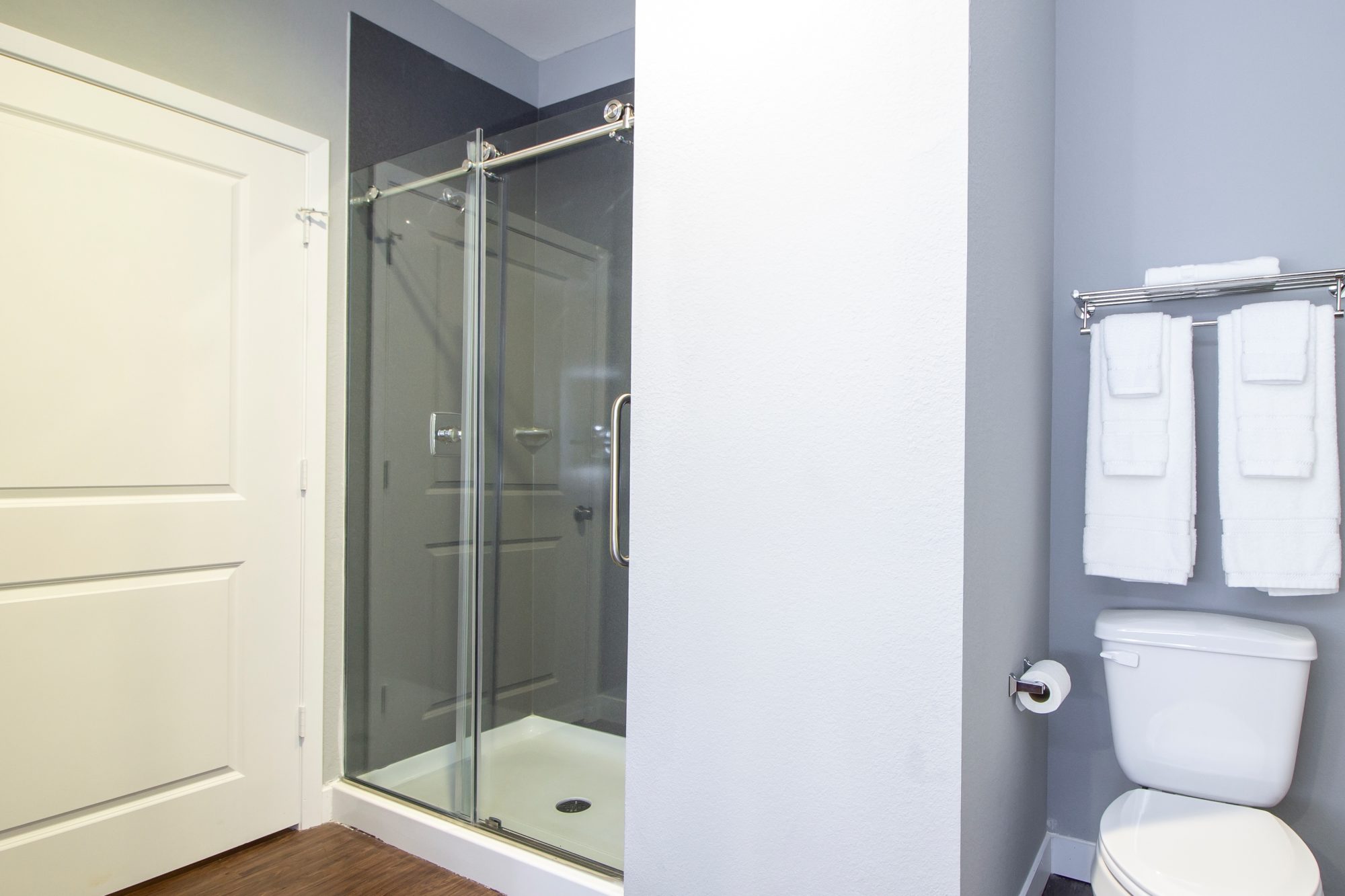 toilet, towel rail and shelf with towels, shower with glass door, laminate flooring