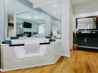 Jacuzzi with bath mat, mirrored walls, vanity unit, mirror, towel rail with towels, hair dryer, laminate flooring