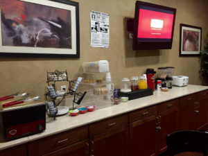 Breakfast display counter with cereal dispensers, breakfast pastries display case, toaster, juice, wall mounted flat screen tv