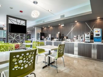 Tables and chairs, breakfast display counter with juice dispenser, coffee machine, waffle machine, microwave, chill cabinet, tiled flooring