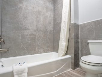 Shower tub with shower curtain, bathmat with bathroom amenities, toilet, laminated flooring