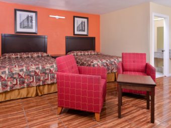 Two queen beds, night stand, easy chairs, occasional table, wall mounted art, laminate flooring, doorway to bathroom