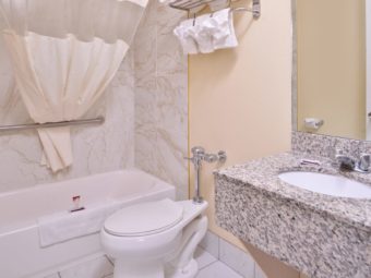 Vanity unit, mirror, towel rail and shelf with towels, shower tub, shower curtain, toilet, tiled flooring