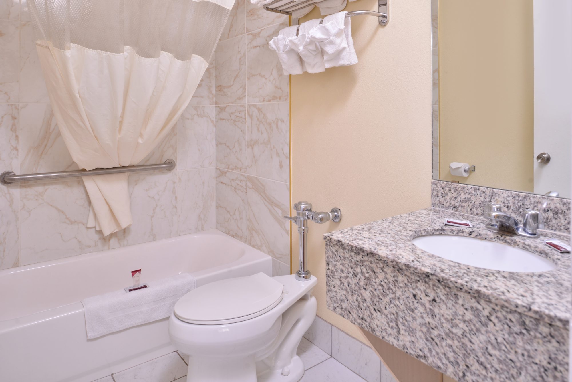 Vanity unit, mirror, towel rail and shelf with towels, shower tub, shower curtain, toilet, tiled flooring