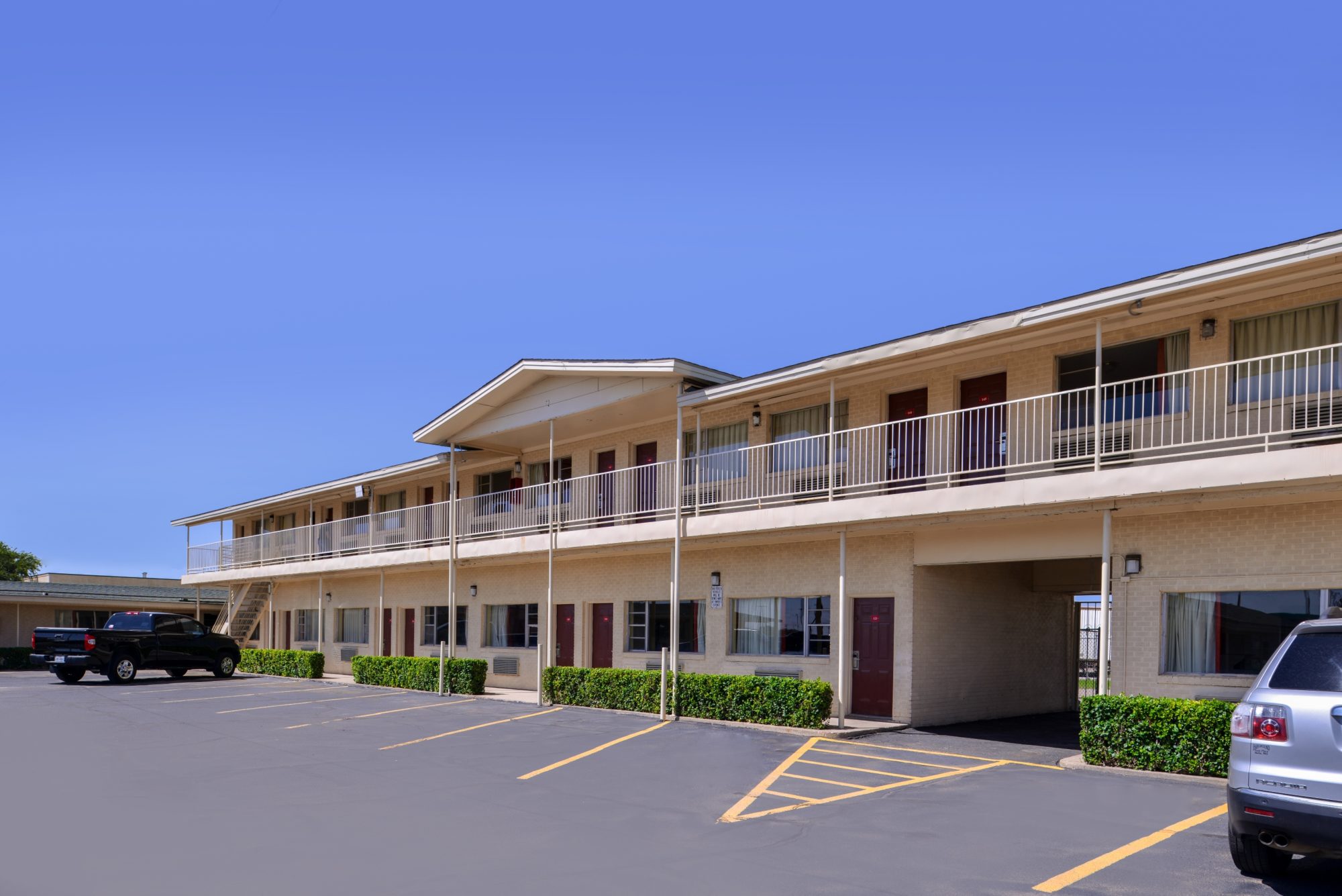 STXLB Exterior 2 Two story building with exterior room entrances, covered walk ways and stairs, small hedges, parking spaces