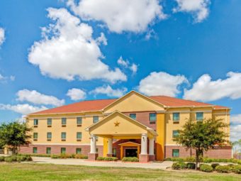 Three story building, hotel entrance with canopied drive through, grassy areas, small trees and shrubs