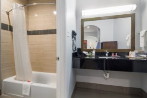 Vanity unit, mirror with overhead light, towel rail with towels, hairdryer, bathroom amenities, doorway to showertub with shower curtain and bathmat