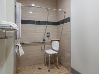 Walk in shower with seat, grab rails, shower curtain, shalf with towels, tiled flooring