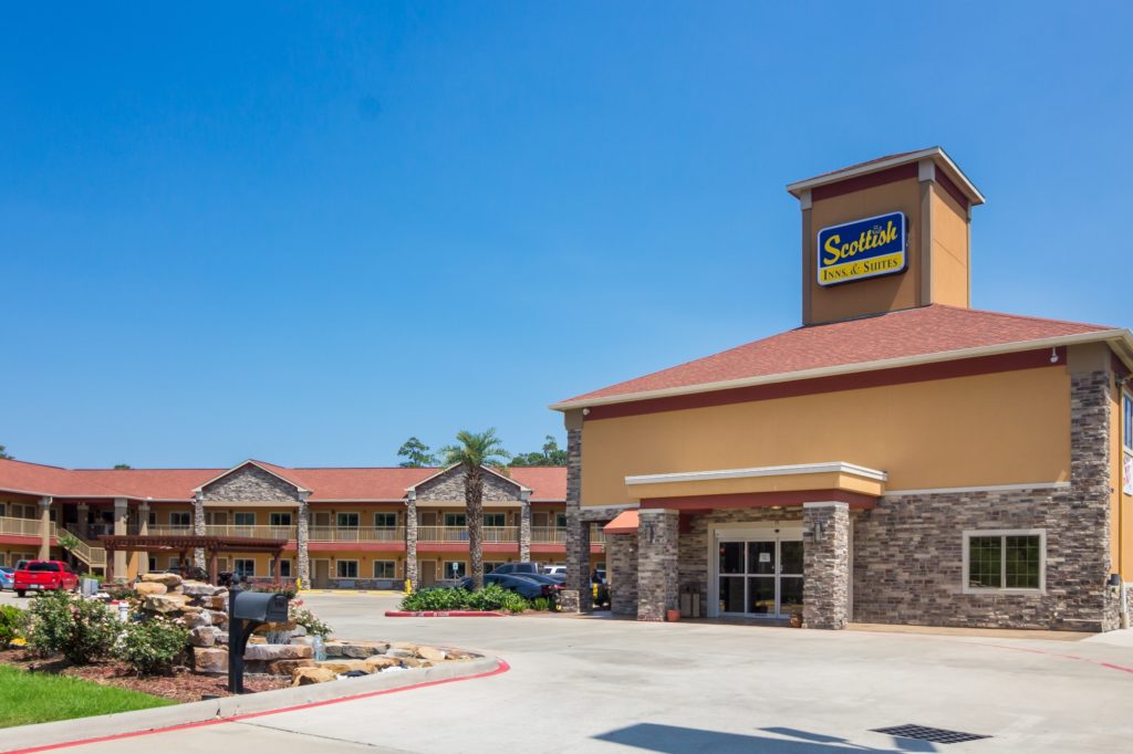 Hotel entrance, parking area, ornamental waterfall, shrubs, two story building with exterior walkways, stairs and room entrances