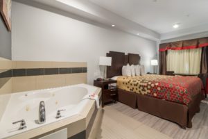 Jacuzzi with tiled surround, king bed, night stands with bedside lamps, telephone and clock, laminate and tiled flooring