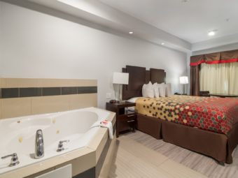 Jacuzzi with tiled surround, king bed, night stands with bedside lamps, telephone and clock, laminate and tiled flooring