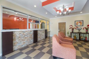 Guest check in desk with glass screens, easy chairs, decorative shelf with floral display, tiled flooring