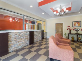 Guest check in desk with glass screens, easy chairs, decorative shelf with floral display, tiled flooring