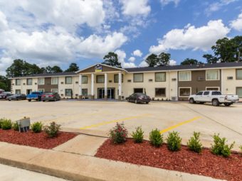 Two story building, canopied hotel entrance, parking spaces, landsacping with small flowering shrubs