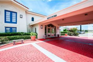 Hotel entrance with canopied drive through, landscaping with small trees and bushes, two story building