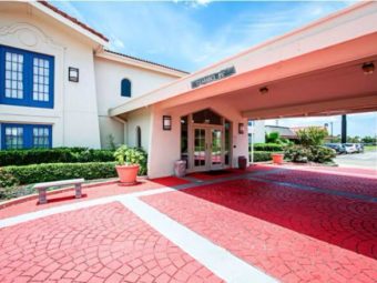 Hotel entrance with canopied drive through, landscaping with small trees and bushes, two story building