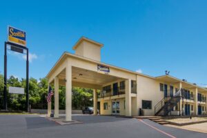 Brand signage, hotel entrance with canopied drive through, two story building with exterior walkways, stairs and guest room entrances, parking spaces