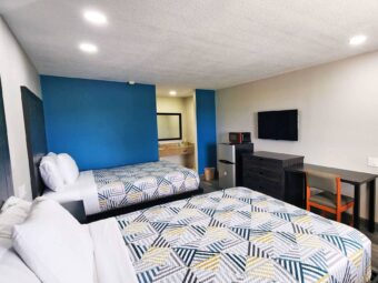 Two queen beds, fridge with microwave, wooden drawer unit, wall mounted TV, desk with chair, alcove with vanity unit and mirror, laminate flooring