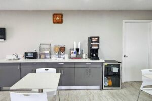 Breakfast options display counter with cereal and coffee machine, toaster oven, fridge with chilled items, milk and juice, tables and chairs, tiled flooring