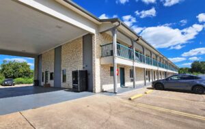 Hotel entrance with drive through canopy, two story building with covered walkways and exterior guest room entrances, parking spaces