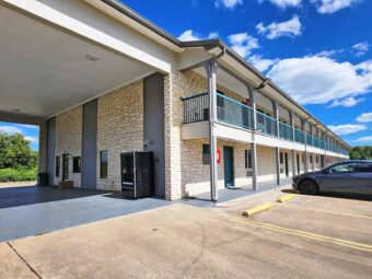 Hotel entrance with drive through canopy, two story building with covered walkways and exterior guest room entrances, parking spaces