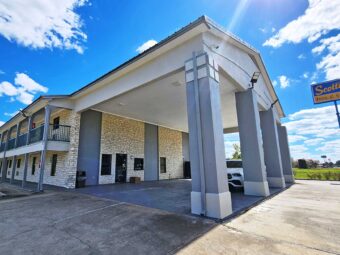 Hotel entrance with drive through canopy, two story building with covered walkways and exterior guest room entrances, brand signage