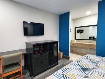 King bed, desk with chair, wall mounted TV, wooden unit with fridge and microwave, alcove with vanity unit, mirror, tiled and laminate flooring