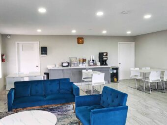 Tables and chairs, sofa and occasional chair, breakfast display counter with cereal and coffee machine, fridge with milk and juice, tiled flooring