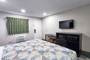 Queen bed, desk with chair, wall mounted TV, wooden unit with microwave and fridge, laminate flooring