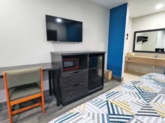 Queen bed, desk with chair, wall mounted TV, wooden unit with microwave and fridge, alcove with vanity unit, mirror and hanging rail, laminate and tiled flooring