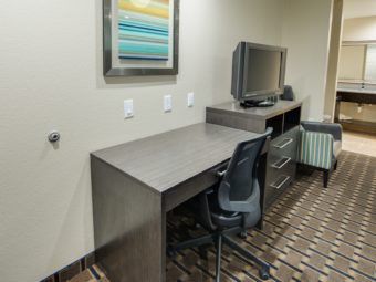 Desk with office chair, art image, wooden drawer unit with tv, easy chair, alcove with vanity unit and mirror, carpet and tiled flooring