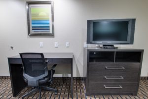 Desk with office chair, art image, wooden drawer unit with tv, carpet flooring