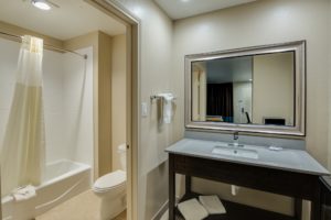 Vanity unit, mirror, towel rail with towels, door way o bathroom, shower tub with shower curtain, toilet, tiled flooring