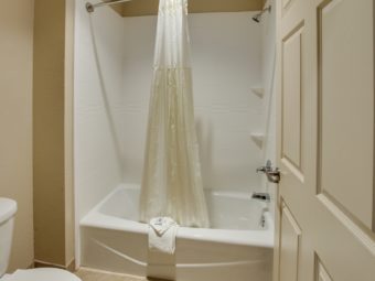 Shower tub with shower curtain, bath mat and bathroom amenities, toilet, tiled flooring