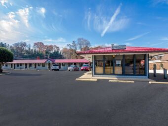 Hotel entrance with guest check in area, single story building with exterior guest room entrances, parking spaces, small tree