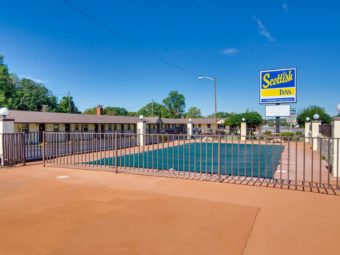 Exterior pool with safety fencing, brand signage, one story hotel building with exterior room entrances and parking spaces